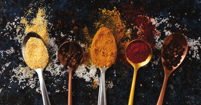 Spoons of ground and whole spices on a dark surface